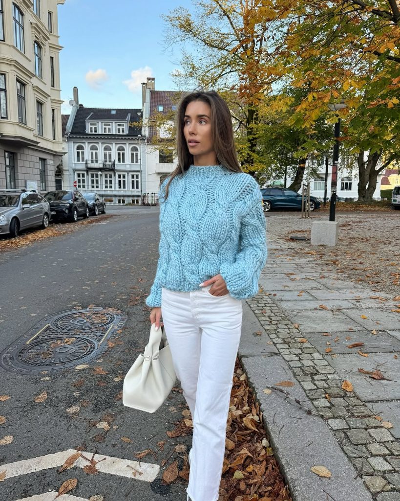 Casual spring outfit featuring a baby blue chunky cable knit sweater, straight-leg white jeans, white and navy sneakers, and cream leather tote bag for a comfortable yet polished everyday look
