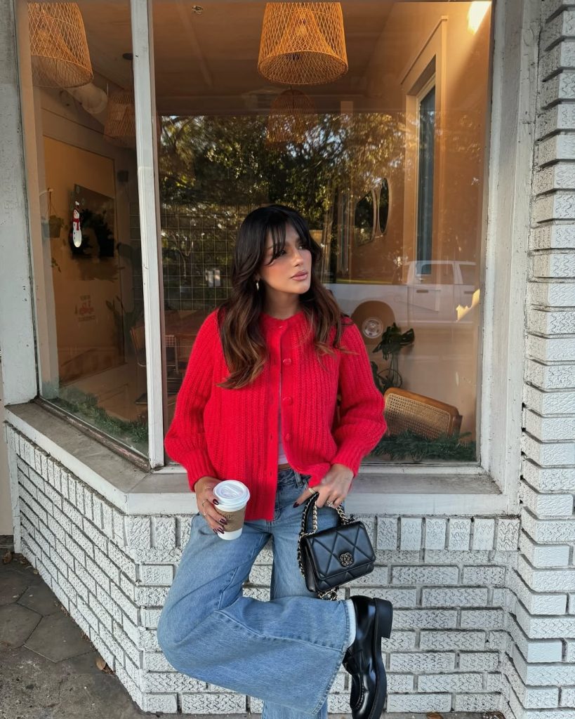 Casual spring outfit featuring a bright red button-up knit cardigan, white tank top, light wash wide-leg jeans, chunky black boots, and quilted black crossbody bag
