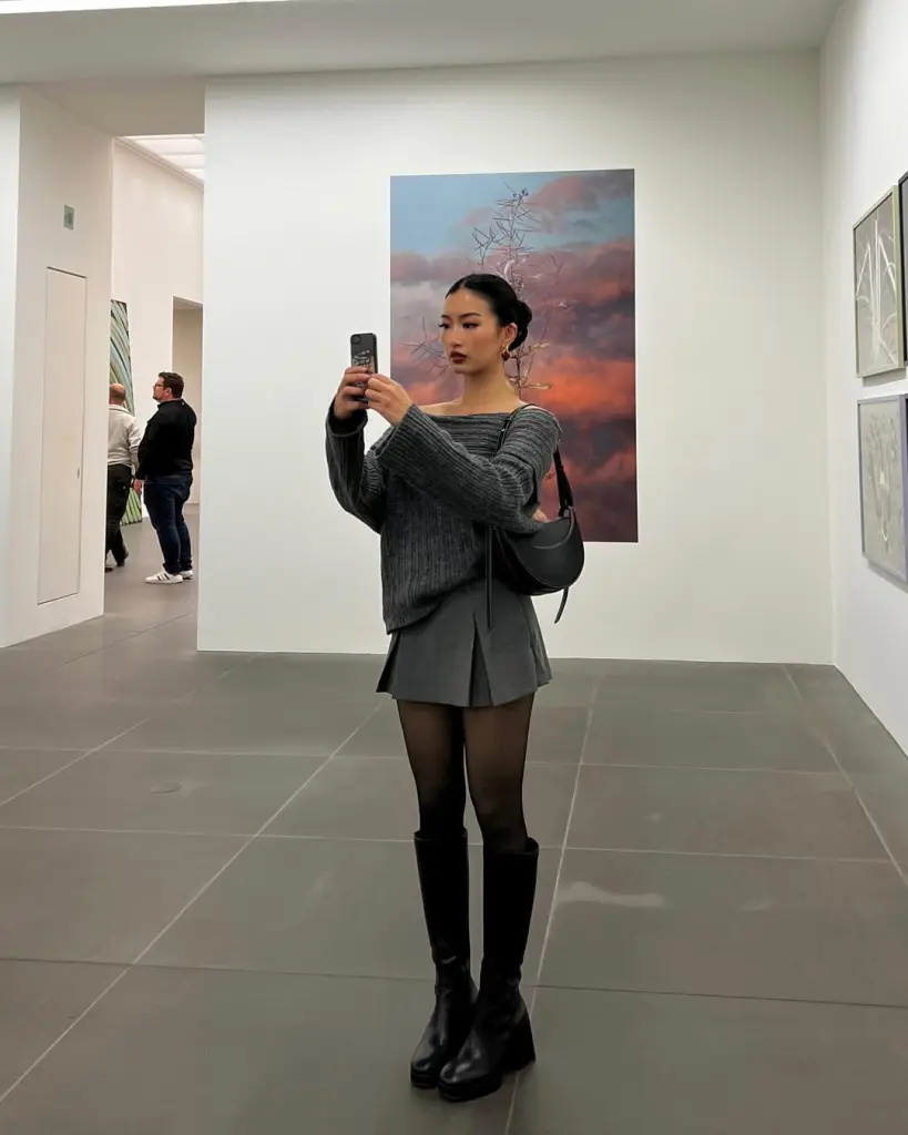 Woman in grey off shoulder sweater with pleated mini skirt and knee high boots