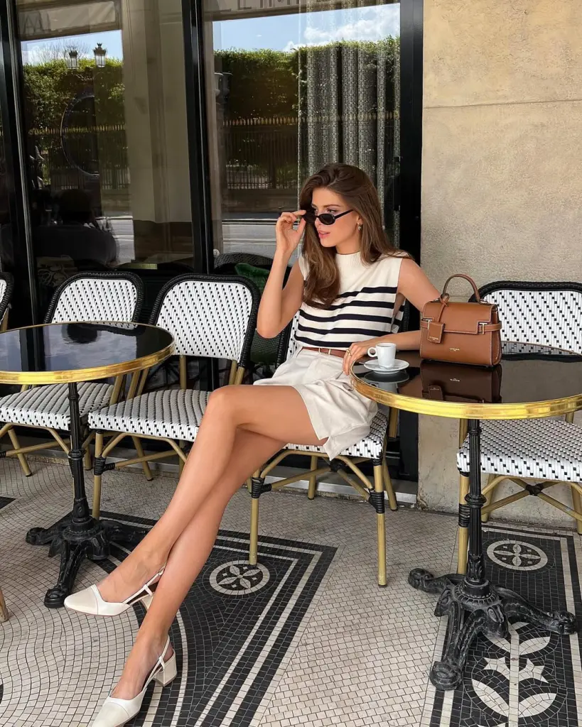 Parisian café old money outfit with white and navy striped sleeveless top, cream belted shorts, white slingback heels and structured tan leather handbag