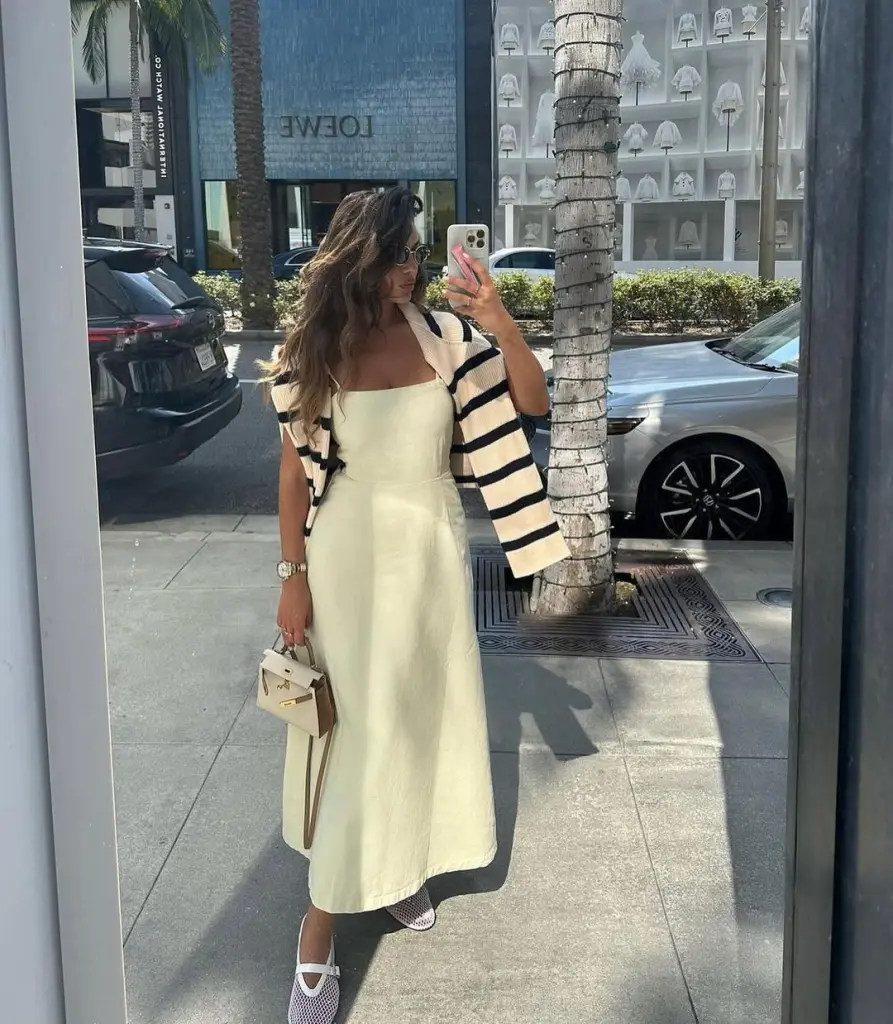 Woman in cream strapless A-line dress with striped cardigan and mesh flats