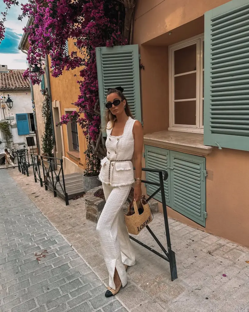 Coastal European old money outfit with white tweed peplum vest, matching wide-leg pants with side slits, two-tone ballet flats and natural straw tote bag