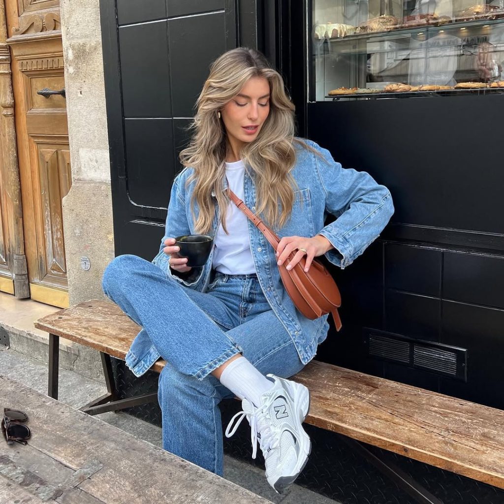 Casual spring outfit featuring a classic denim-on-denim look with oversized light wash jean jacket, white t-shirt, straight-leg blue jeans, white sneakers with crew socks, and brown leather crossbody bag