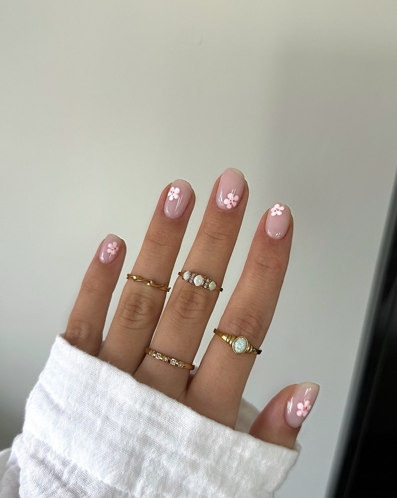 Short pink nails with white flower details and gold rings