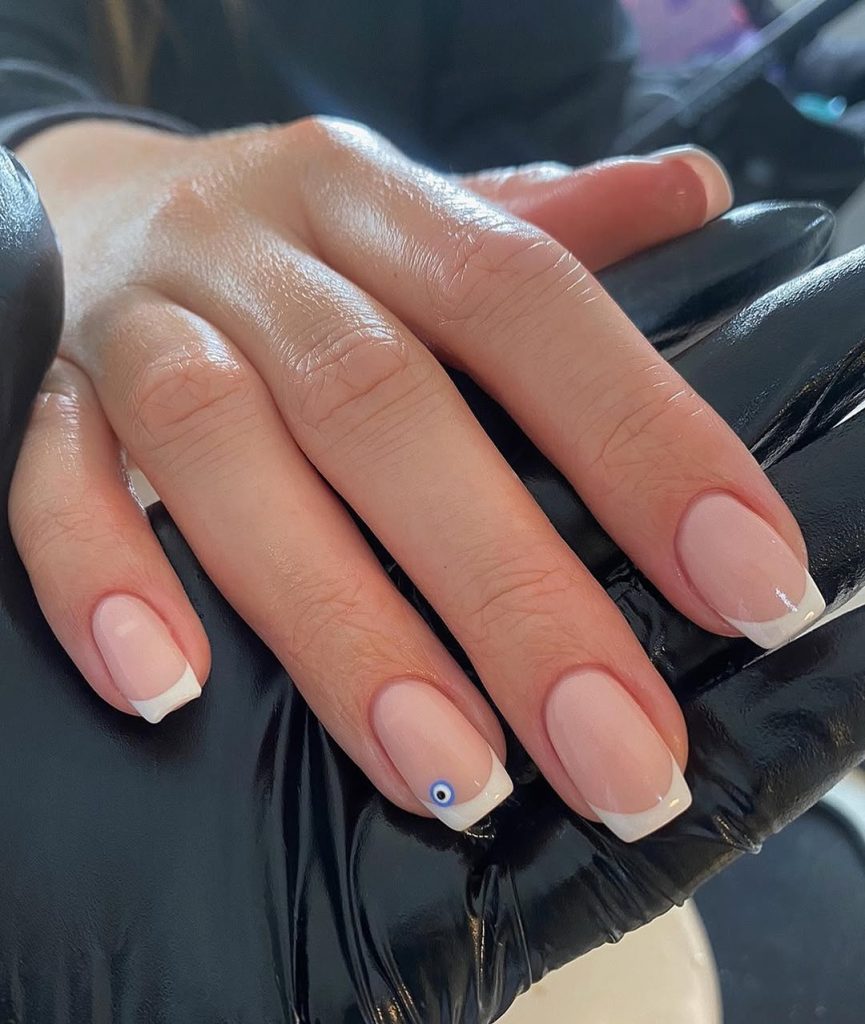 Classic French manicure with tiny blue evil eye accent nail
