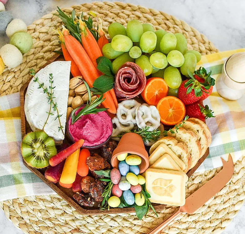 Colorful Easter charcuterie board featuring fresh fruits, cheese, meats, and candies arranged on a wooden platter with seasonal accents and festive spring colors