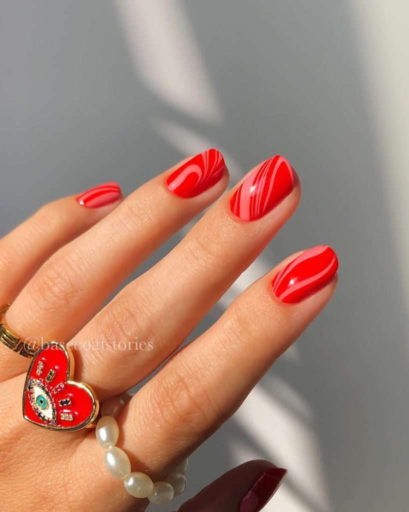 Short oval nails with bright red polish and glossy marble swirl design pattern

