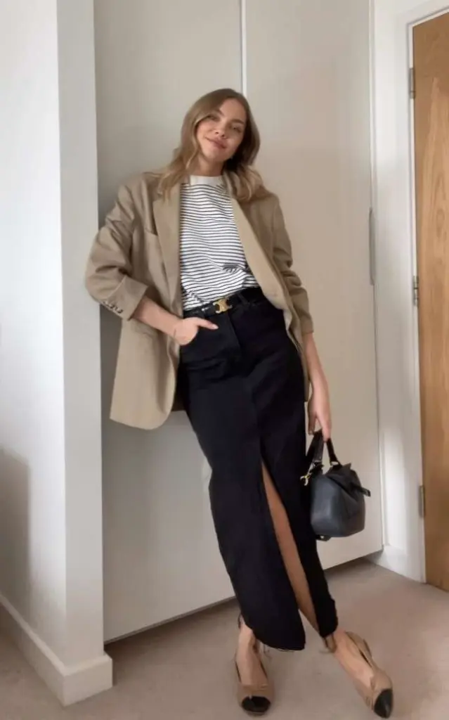 Business casual outfit with beige oversized blazer, black and white striped top, black split maxi skirt, black belt, nude cap-toe flats and small black handbag
