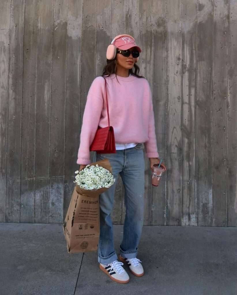 Casual spring outfit with pink oversized sweater, light wash jeans, white and black Adidas sneakers, pink baseball cap and red shoulder bag
