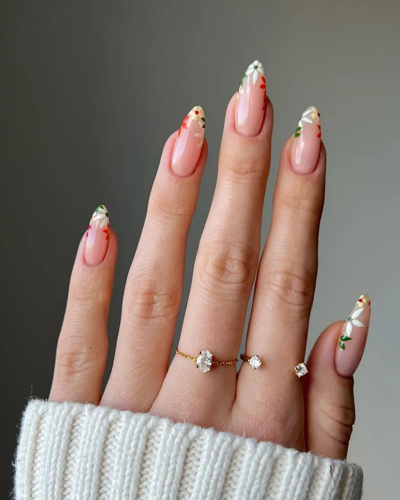 Almond shaped nude pink nails with colorful French tips featuring white, red and yellow floral designs
