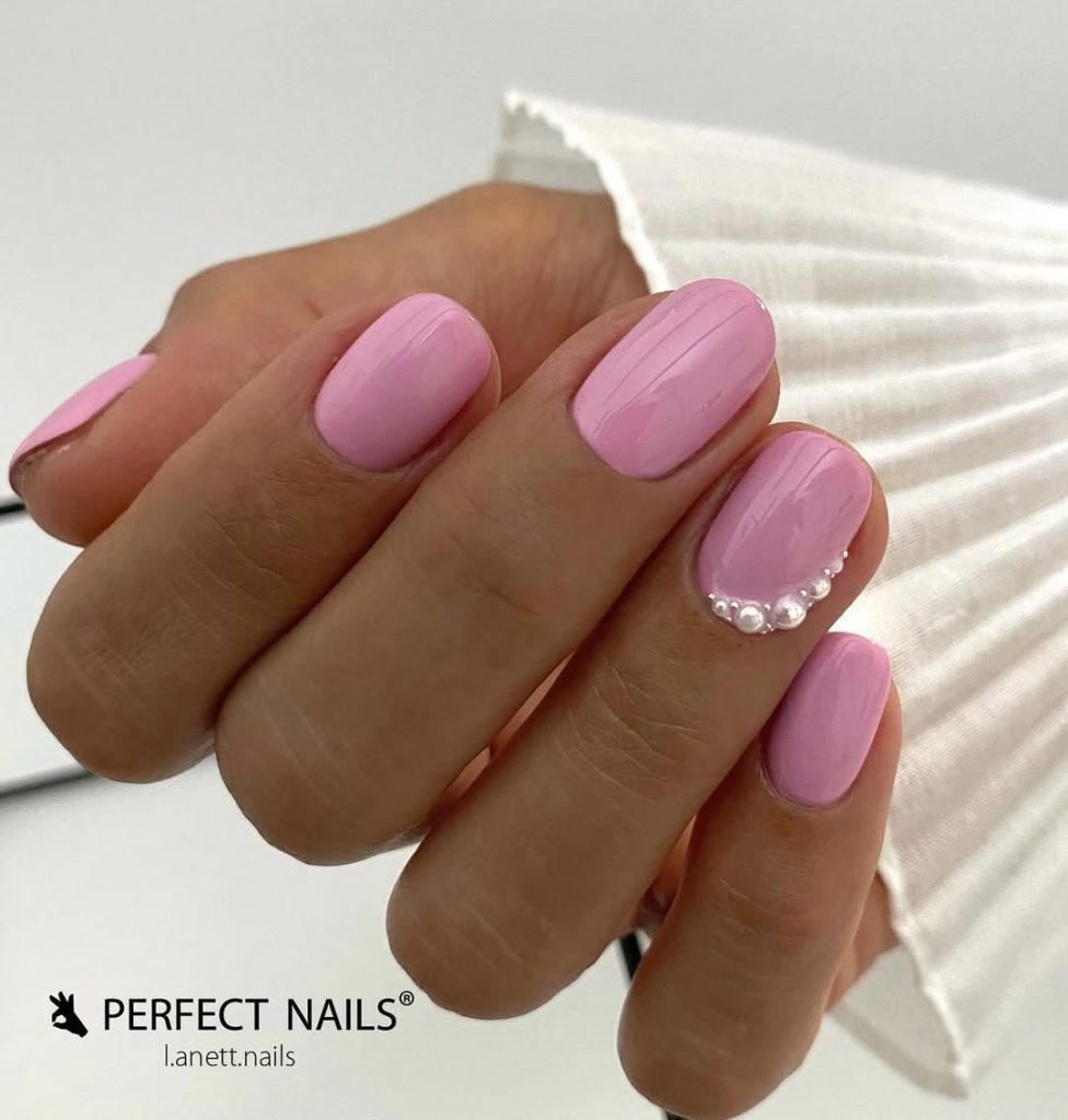 Short square nails with soft lilac pink polish and pearl embellishments on ring finger