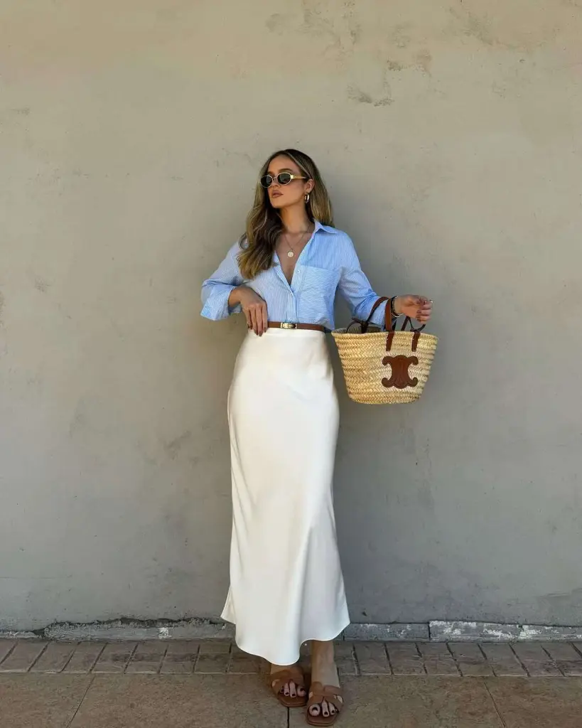 Classy spring outfit with blue striped button-down shirt, cream maxi skirt, brown leather sandals and straw tote bag