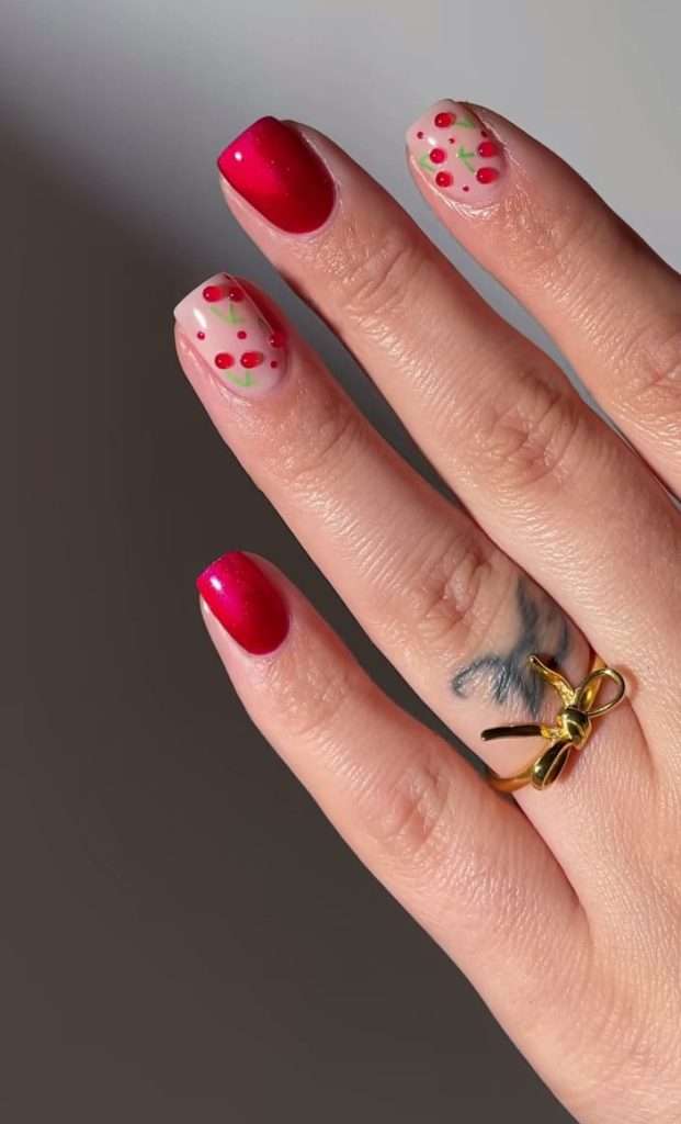 Short square nails with metallic red polish and clear base accent nails featuring 3D cherry designs
