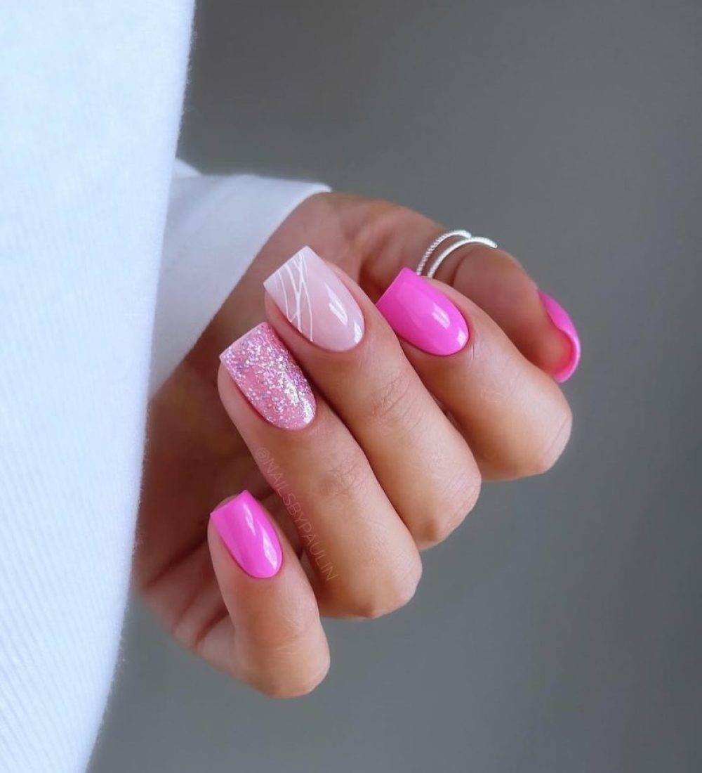 Short square nails with mix of hot pink polish, pink glitter nail, and milky pink base with white swirl design