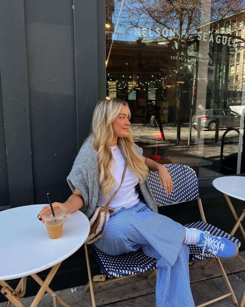 Casual spring outfit with gray oversized cardigan, white t-shirt, blue and white striped wide leg pants, blue sneakers and brown crossbody bag
