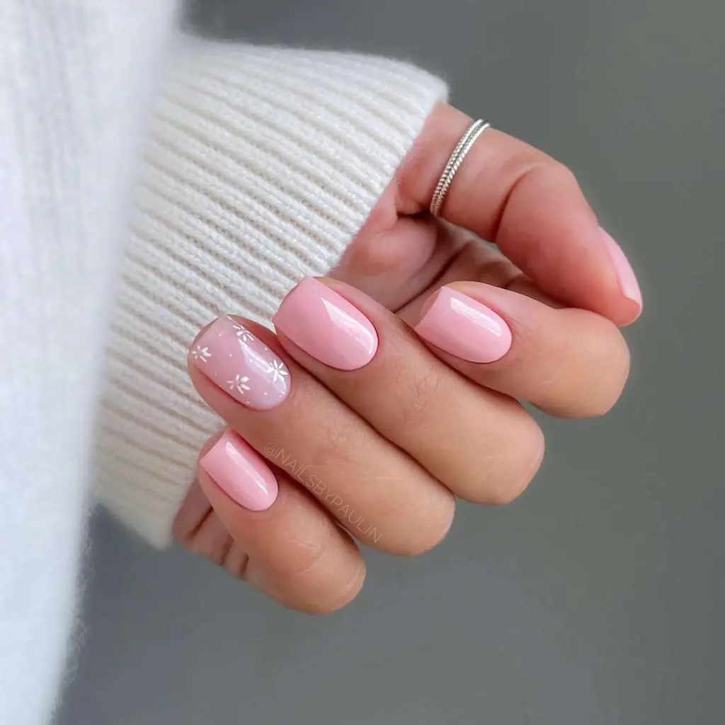 Short square nails in glossy pink polish with white daisy detail on accent nail
