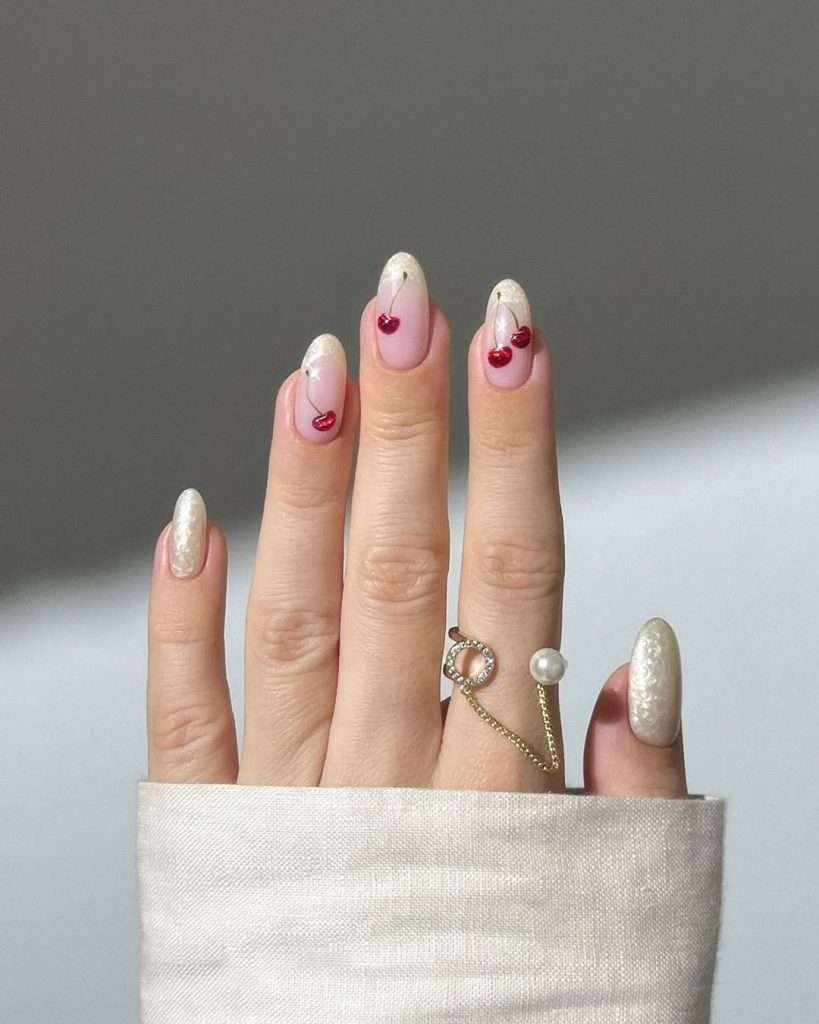 Long almond nails with pink base, pearl white tips, and red cherry designs