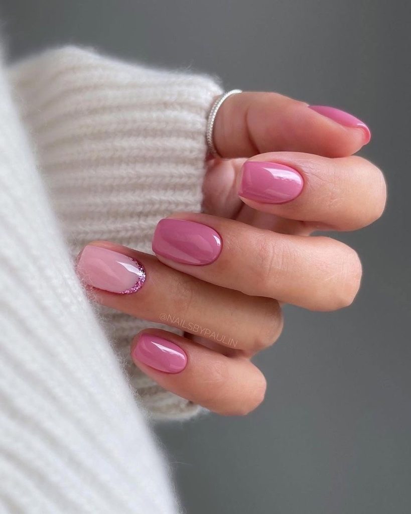 Short nails with rose pink polish and translucent base with pink glitter border on ring finger
