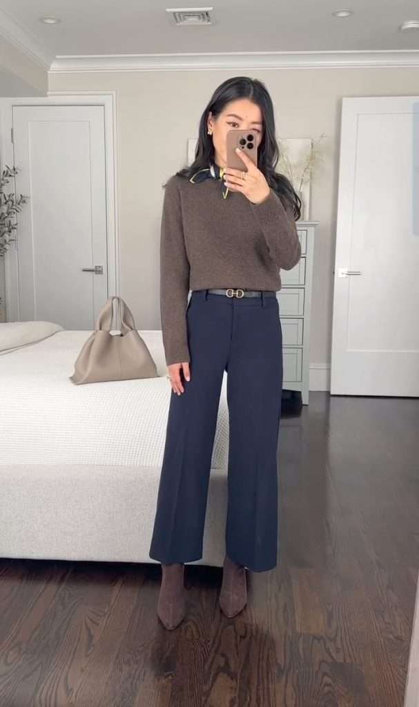 Business casual outfit with brown v-neck sweater, white collar shirt, navy wide-leg trousers, designer belt and brown suede boots with beige handbag