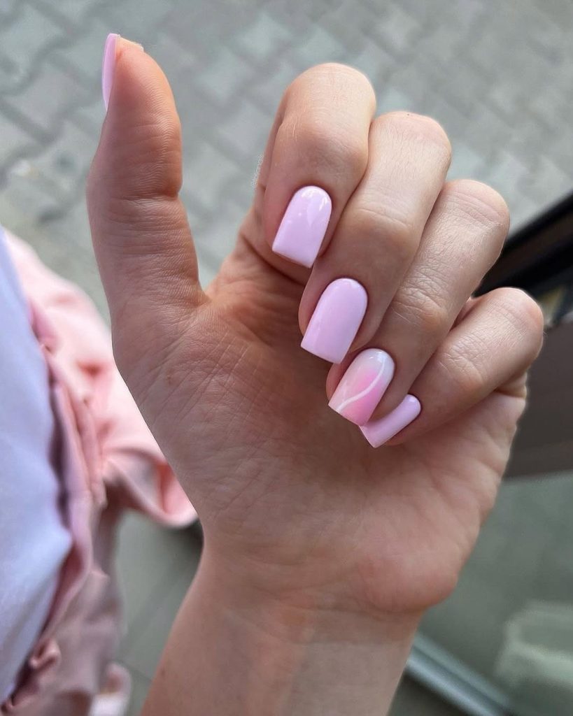 Short square nails with pastel pink polish and a pink ombré and a white curved line design on ring finger
