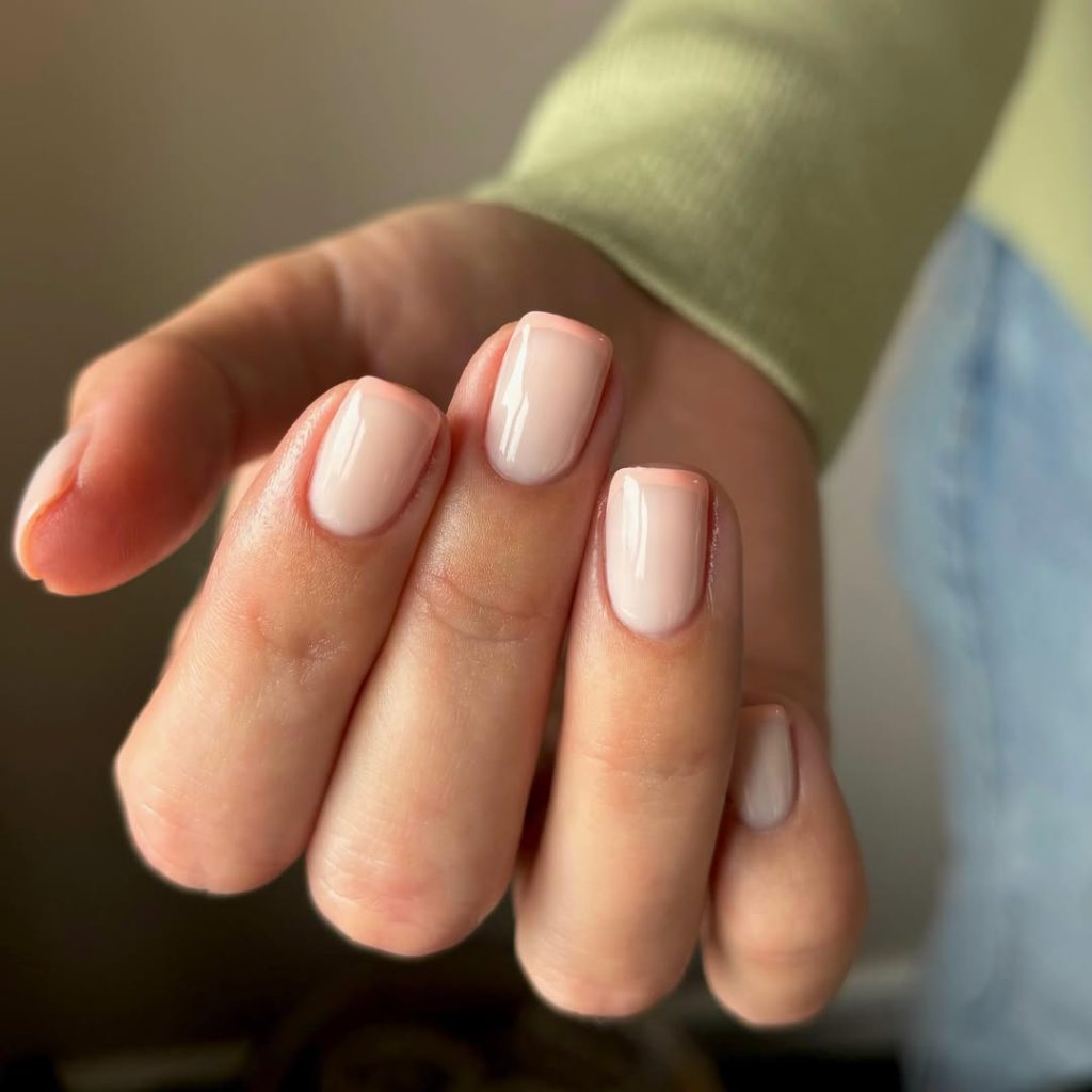 Short square nails with clear base and delicate peach French tips creating a subtle spring elegance