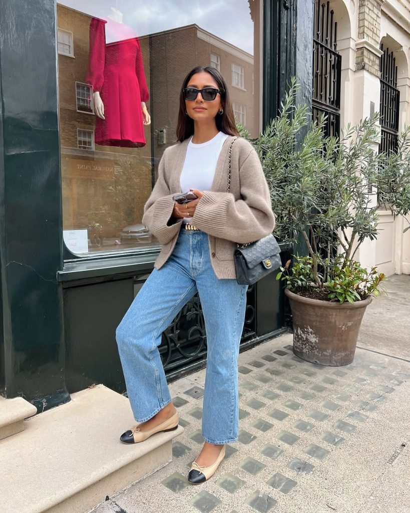 Classic spring outfit with beige oversized cardigan, white t-shirt, straight leg jeans, beige and black cap-toe ballet flats, gold belt and quilted grey shoulder bag
