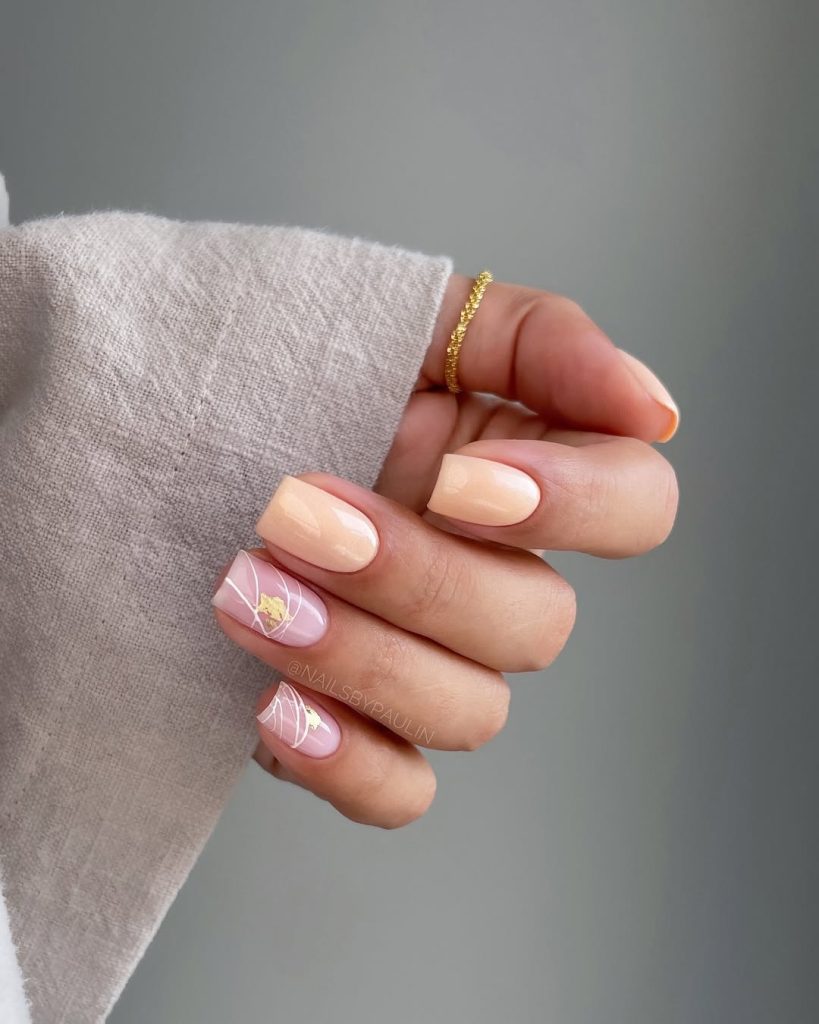 Short square nails with peach base color and pink accent nails with gold foil and white swirl details
