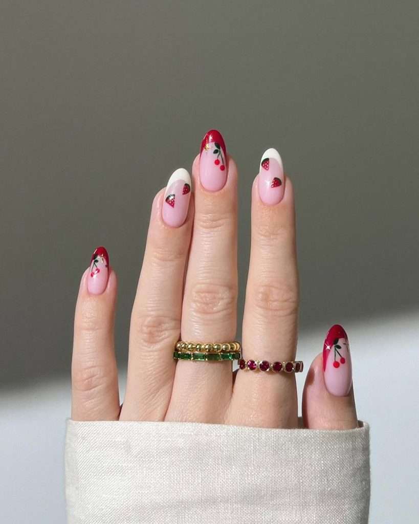 Almond nails with pink base, red French tips, strawberry and cherry nail art details
