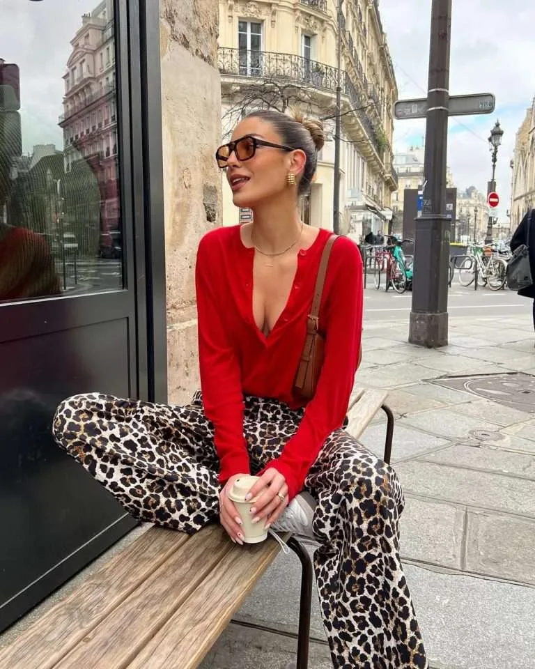 spring outfit with red button-up cardigan, leopard print wide leg pants, white sneakers, tortoise sunglasses and brown bag