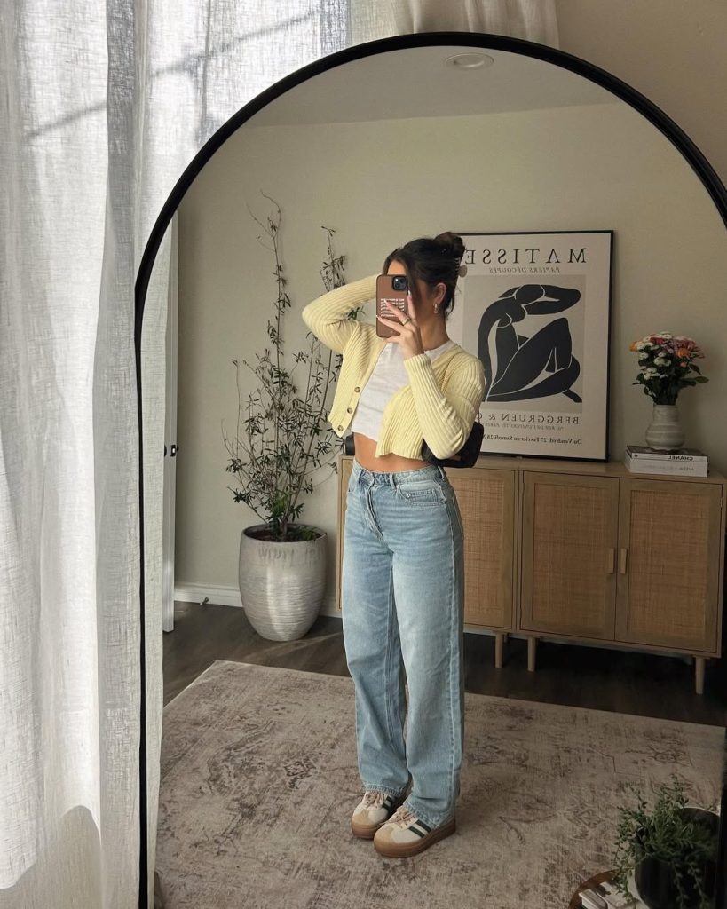 Casual spring outfit with pale yellow cropped cardigan, white crop top, light wash baggy jeans, platform sneakers and sleek updo hairstyle
