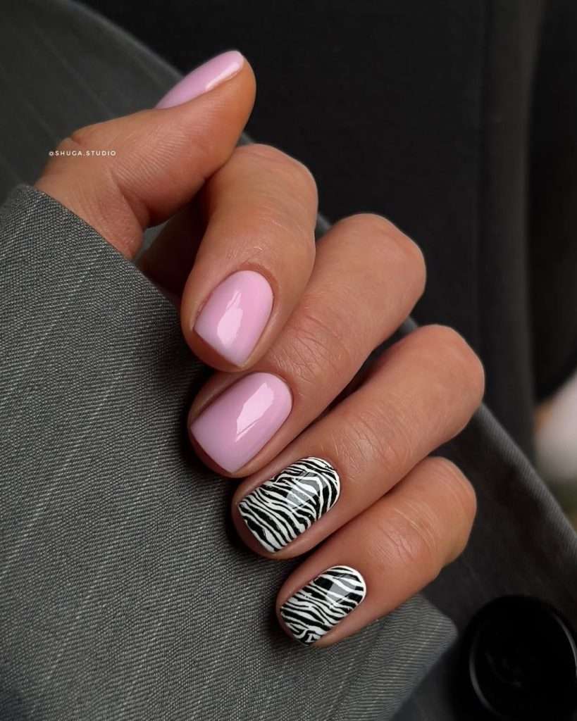Short square nails with light pink polish and two accent nails featuring black and white zebra print
