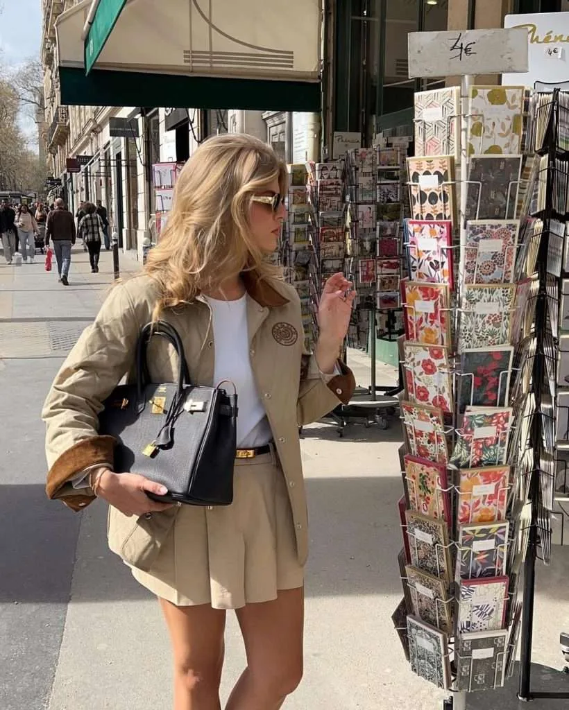 Classy spring outfit with beige quilted jacket, matching pleated shorts, white t-shirt, and black Hermès bag
