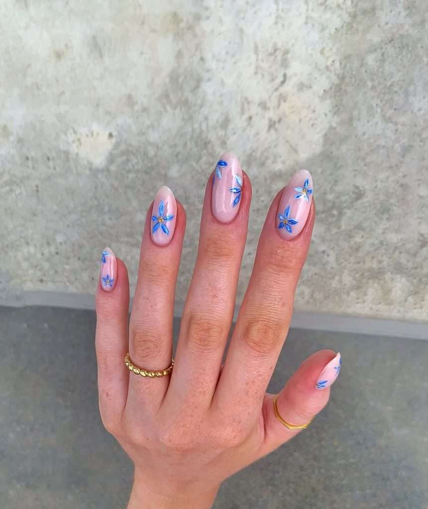 Long almond nails with pink base and blue flower designs with gold centers
