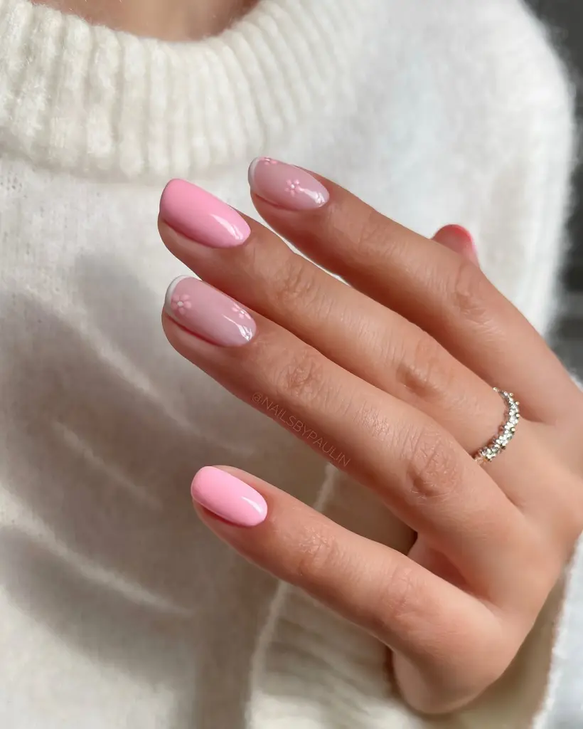 Short oval nails alternating between solid pink and sheer pink base with small white daisy flower accents
