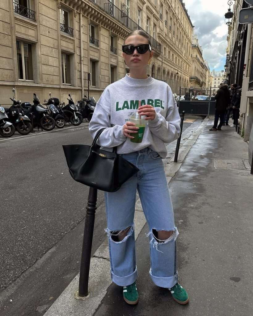 casual outfit with gray logo sweatshirt, light wash ripped jeans, green suede sneakers and black structured tote bag
