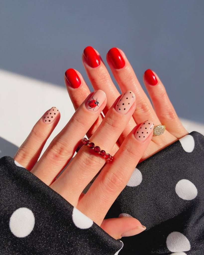 Short oval nails with red polish and nude base accent nails featuring black polka dots and ladybug nail art
