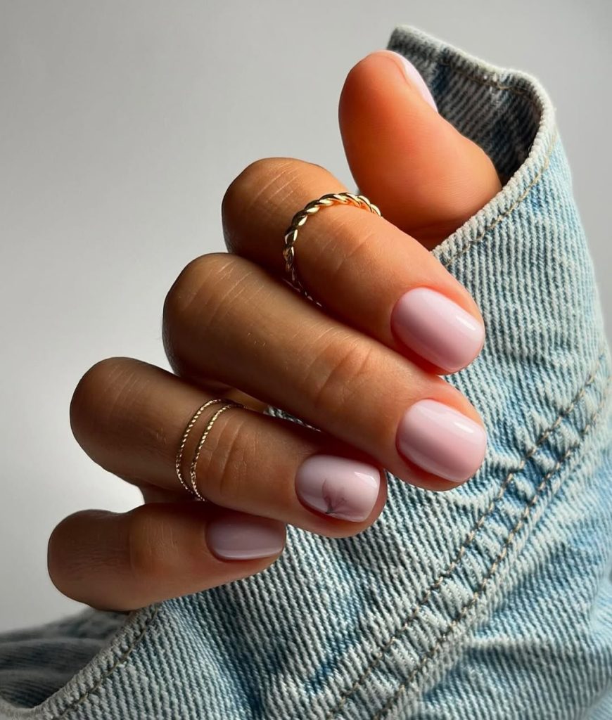 Short nails with sheer baby pink polish and subtle pink flower accent on ring finger