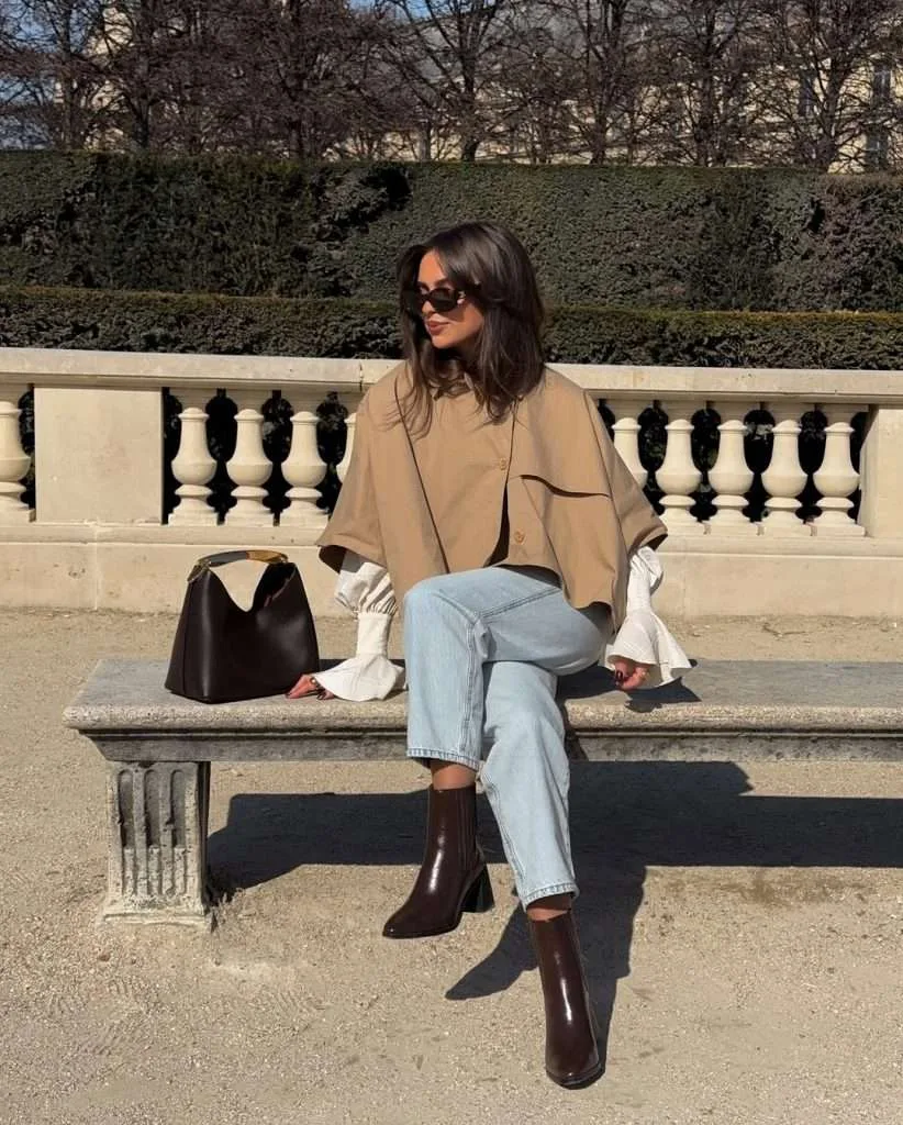 Classy spring outfit with camel cape trench, white ruffle sleeve top, light wash jeans, brown leather boots and black leather bag
