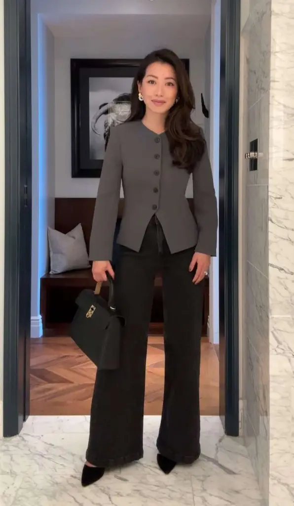 Business casual outfit with grey collarless fitted jacket, dark wide-leg jeans, black pointed heels and black structured handbag
