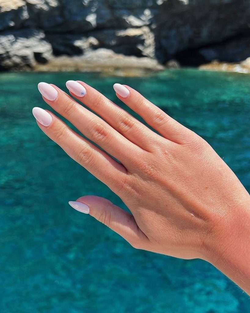 Long almond nails with milky white polish and blue evil eye accent
