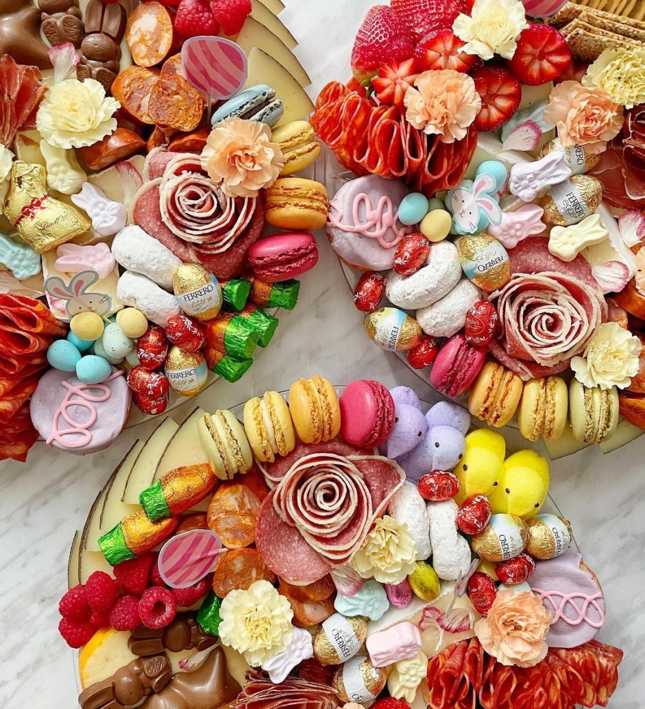 Circular Easter charcuterie arrangement featuring colorful macarons, chocolate eggs, salami roses, strawberries, and bunny-shaped treats on elegant wooden boards