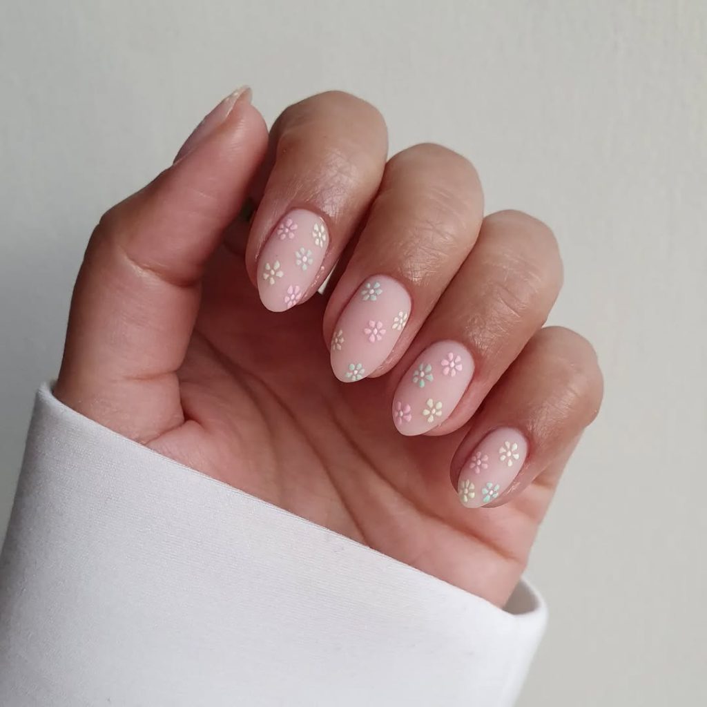 Almond shaped pink nails with small multicolored daisy flower pattern in white, blue and pink throughout