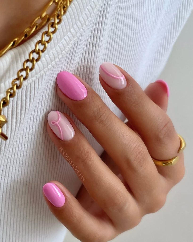 Short oval nails with candy pink polish on some nails and sheer base with pink curved line designs on others
