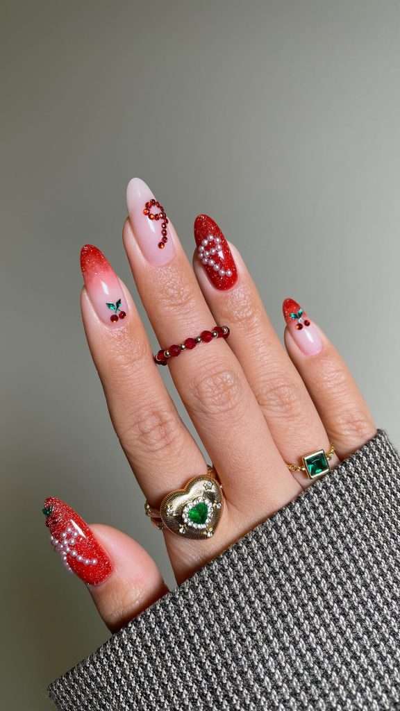 Long almond nails with red glitter polish, pearl details and pink base with cherry nail art and rhinestone accents
