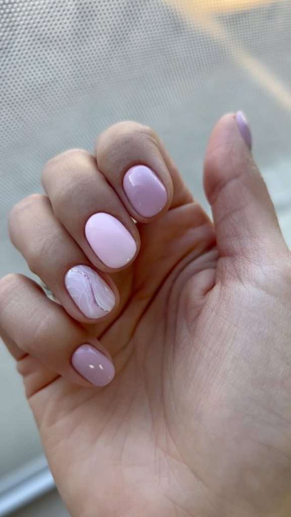 Short square nails with light pink polish and one accent nail featuring white marble design with glitter line
