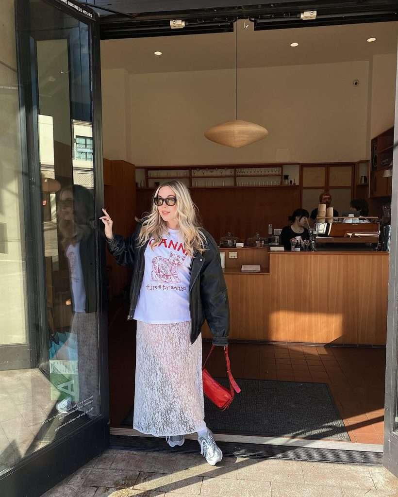 spring outfit with black leather jacket, white cat graphic t-shirt, white lace maxi skirt, gray sneakers and red leather shoulder bag

