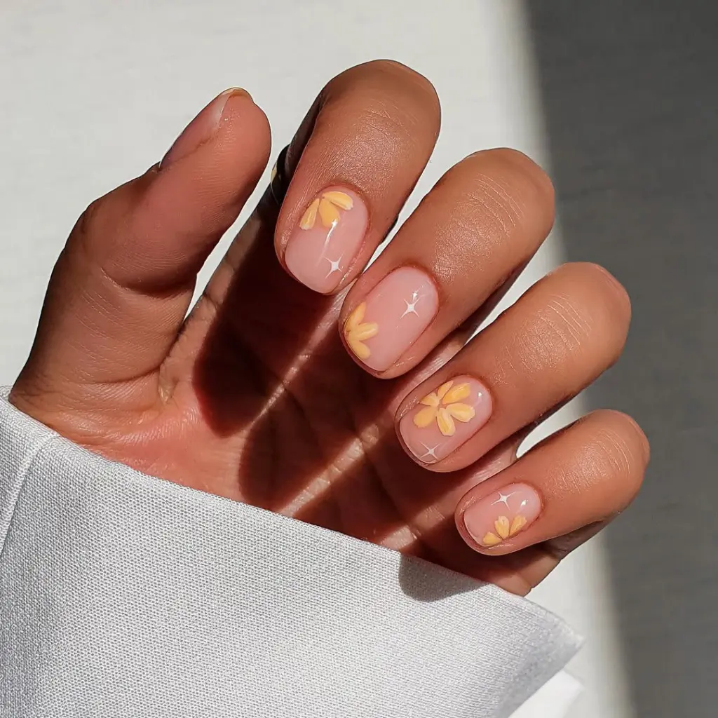 Short square nails with transparent pink base featuring yellow daisy flowers and white star sparkle accents
