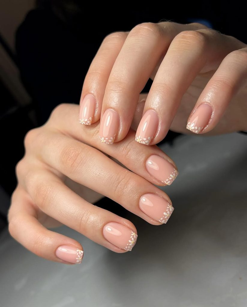 Short square nails with glossy nude pink base and delicate white daisy flower accents along the tips
