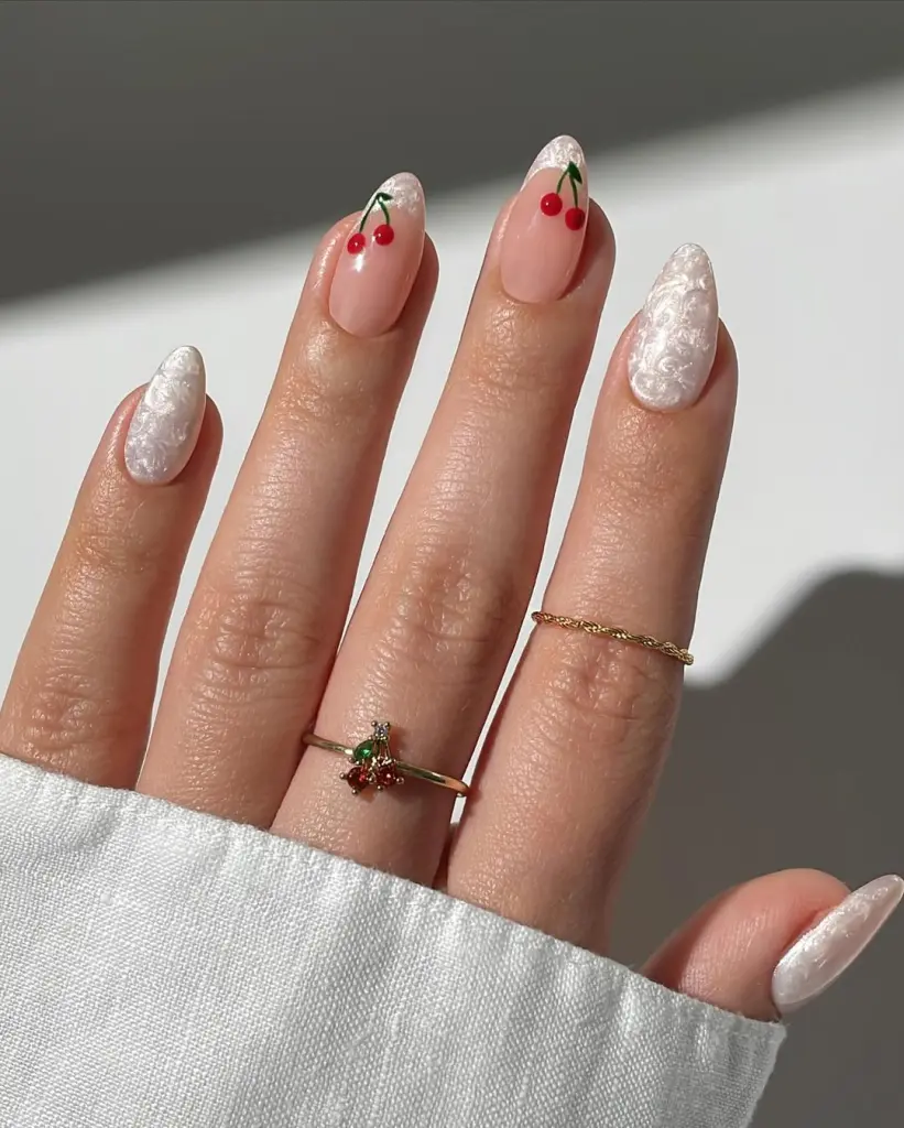 Almond shaped nails with pink base and white textured accent nails featuring small red cherry designs with green stems