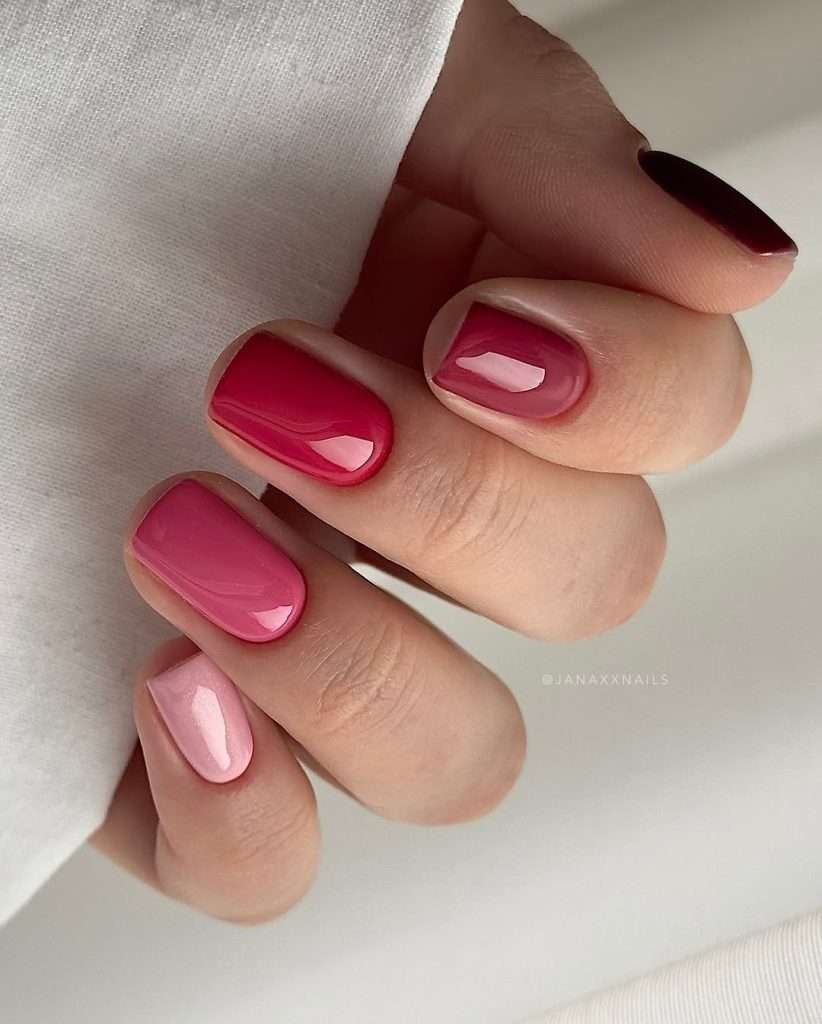 Short square nails with each nail painted in a different shade of pink, ranging from metallic light pink to deep raspberry
